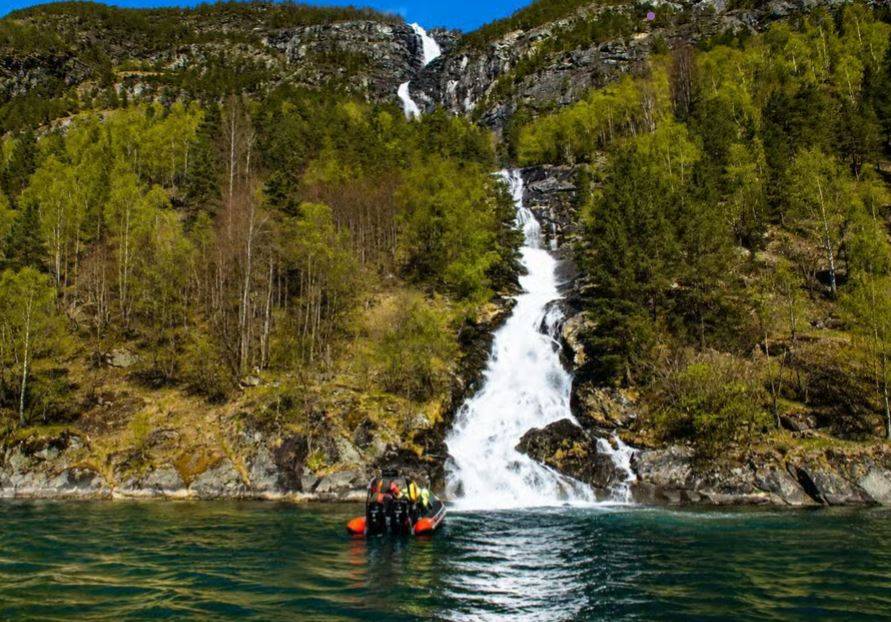 A RIB boat at the foot of a waterfall on the Nærøyfjord near Flåm.